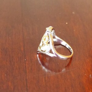 May include: A silver ring with a gold design in the shape of a heart. The ring is on a wooden surface.