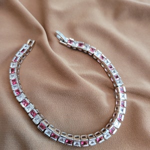 May include: A silver bracelet with alternating pink and white square-shaped stones.