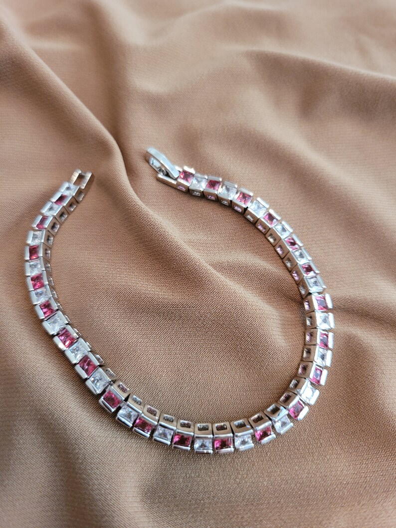 May include: A silver bracelet with alternating pink and white square-shaped stones.