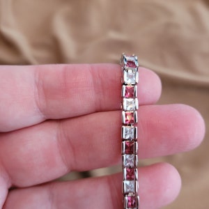 May include: A silver bracelet with alternating clear and pink square-shaped stones.