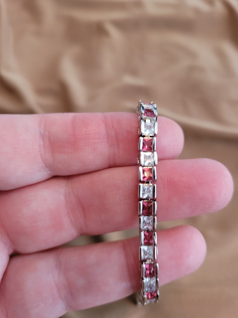 May include: A silver bracelet with alternating clear and pink square-shaped stones.