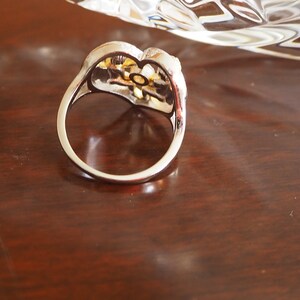 May include: A silver ring with a gold-toned flower design. The ring is set with clear stones.