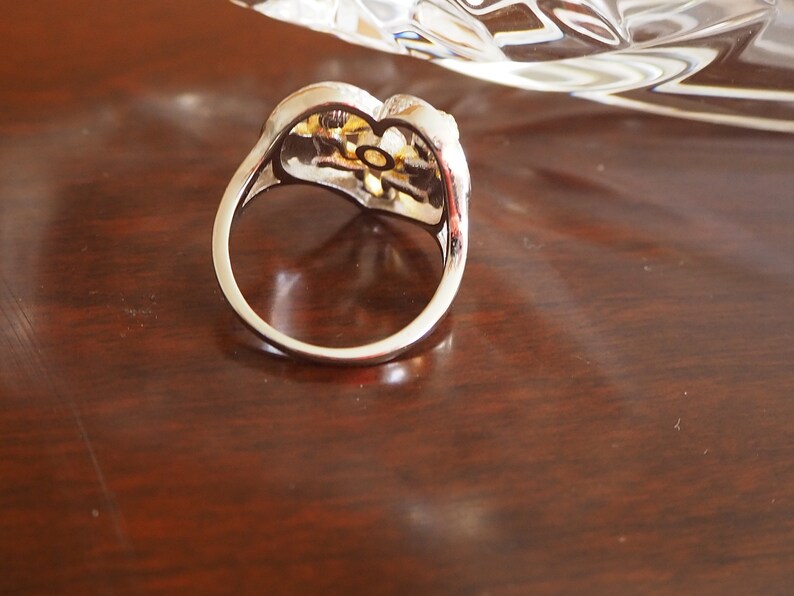 May include: A silver ring with a gold-toned flower design. The ring is set with clear stones.