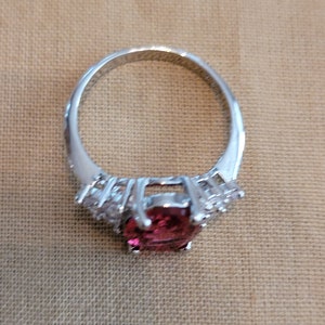 May include: A silver ring with a large, round, pink gemstone surrounded by smaller, clear gemstones.