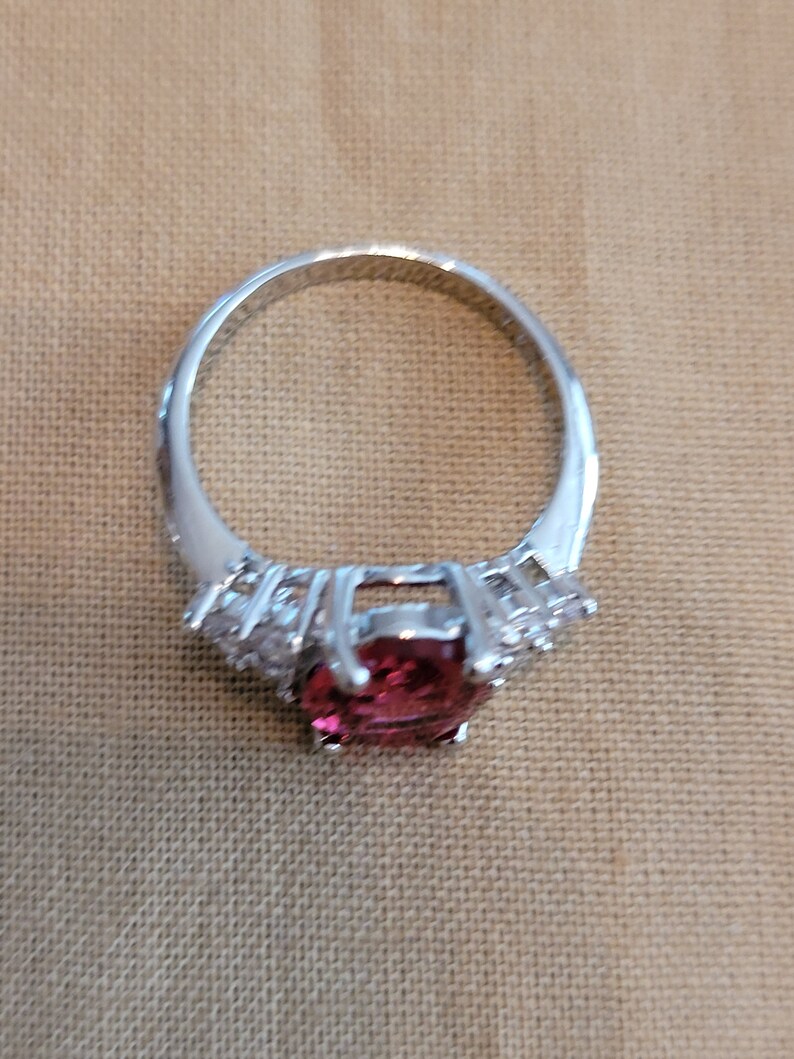 May include: A silver ring with a large, round, pink gemstone surrounded by smaller, clear gemstones.