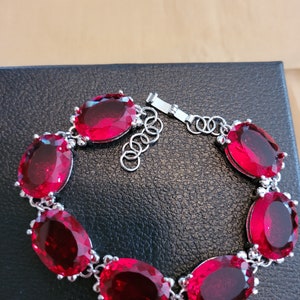 Puede incluir: Un brazalete de plata con cierre de cadena y seis grandes piedras preciosas rojas de forma ovalada.