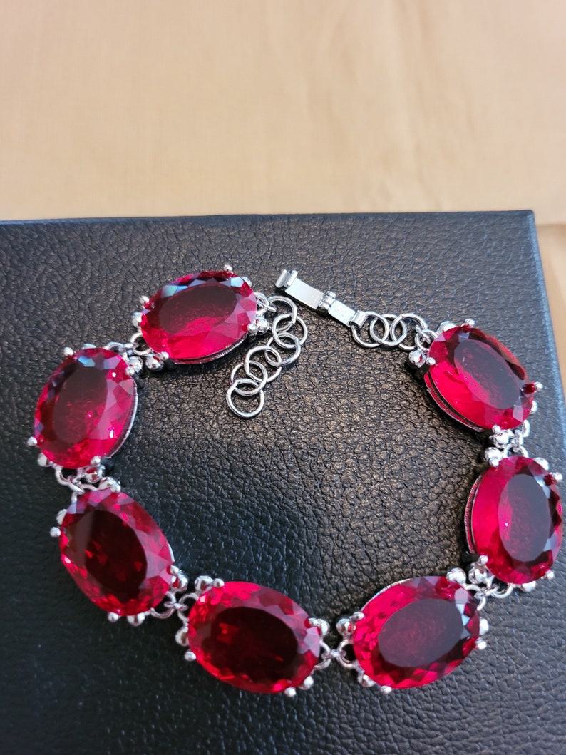 Puede incluir: Un brazalete de plata con cierre de cadena y seis grandes piedras preciosas rojas de forma ovalada.