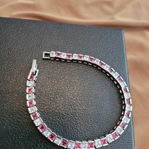 May include: A silver bracelet with alternating clear and pink square-shaped stones.