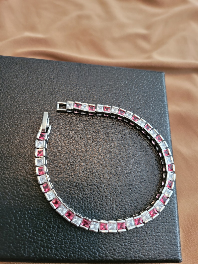 May include: A silver bracelet with alternating clear and pink square-shaped stones.