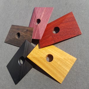 Könnte beinhalten: Fünf Holzblöcke in verschiedenen Farben, jeder mit einem runden Loch in der Mitte. Die Farben sind Schwarz, Dunkelbraun, Hellbraun, Rot und Lila.