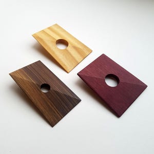 Op de afbeelding: Drie houten plaquettes met een gat in het midden. De plaquettes zijn in verschillende kleuren: naturel hout, donkerbruin en bordeauxrood.