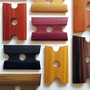 May include: Assortment of eight wooden tools with two holes each. The tools are made of different types of wood, including black, brown, red, and yellow wood. The tools are all the same size and shape.