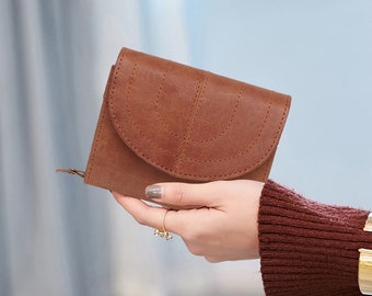 May include: A brown leather wallet with a unique stitched design. The wallet is folded in half and has a zipper on the side.