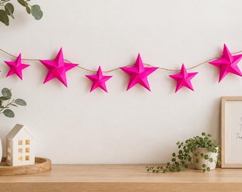 May include: A garland featuring six bright pink, three-dimensional paper stars strung along a thin, natural-coloured twine. The stars vary slightly in size and are evenly spaced, creating a vibrant, geometric decoration for a wall or shelf.
