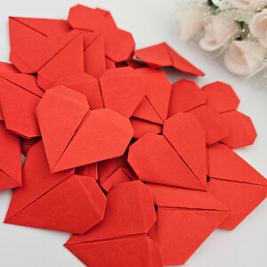 May include: A pile of red origami hearts, folded from paper, on a white surface.