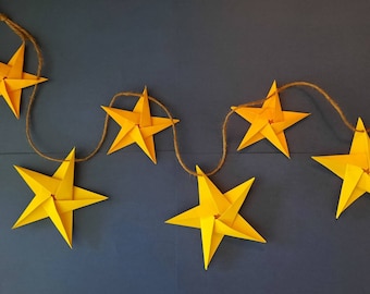 May include: A string of yellow paper stars connected with twine. The stars are folded into a 3D shape and are hanging against a dark blue background.