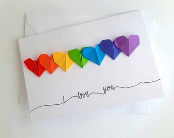 May include: A white card with a rainbow of origami hearts and the text "I love you" written in black ink.