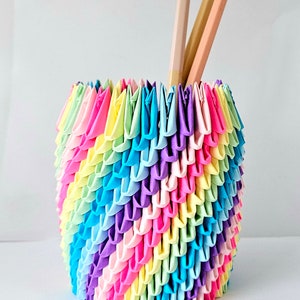 May include: A rainbow origami pencil holder made of folded paper. The holder is filled with two wooden pencils.