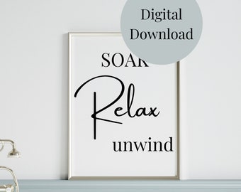 May include: A white framed print with black text that reads "SOAK Relax unwind" in a bathroom setting with a white bathtub and silver faucet.