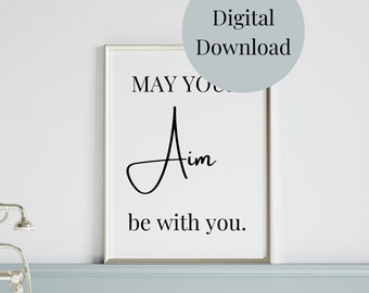 May include: A white framed printable with black text that reads "May your aim be with you."