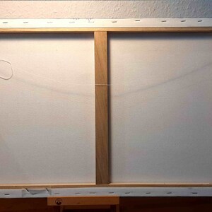 May include: The back of a stretched canvas painting with a wooden frame. The canvas is white and has a string attached to it for hanging.