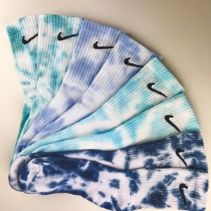 Peut inclure: Un ensemble de six chaussettes tie-dye dans des tons de bleu et de vert avec un logo Nike swoosh noir sur chaque chaussette.