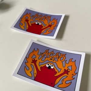 May include: A red cartoon character with big eyes is on fire. The flames are orange and yellow and spell out the word "AGAB". The character is on a purple background.