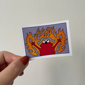 May include: A red cartoon character with big eyes and a wide mouth is engulfed in flames. The flames are orange and yellow and spell out the word "ACAB" in a stylized font.