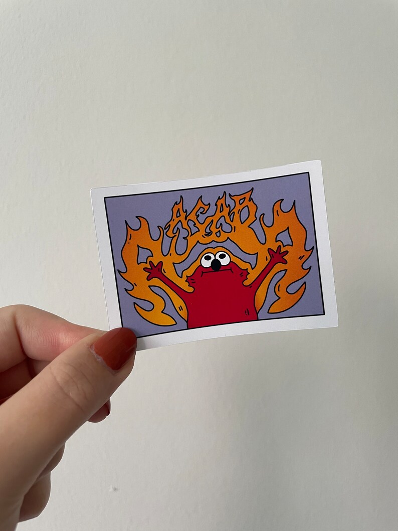 May include: A red cartoon character with big eyes and a wide mouth is engulfed in flames. The flames are orange and yellow and spell out the word "ACAB" in a stylized font.