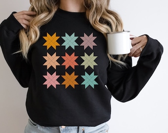 May include: Black sweatshirt with a pattern of nine colorful stars. The stars are made up of a series of intersecting lines, creating a geometric design.