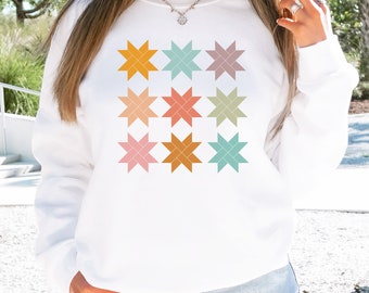 May include: White sweatshirt with a colorful geometric star pattern design. The stars are in shades of orange, yellow, pink, green, and blue.