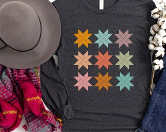 May include: Dark grey long-sleeve shirt with a colorful star pattern. The stars are in shades of orange, pink, blue, and green. The shirt has a crew neck and is made of a soft material. The text "Dark Grey Heather" is at the bottom.