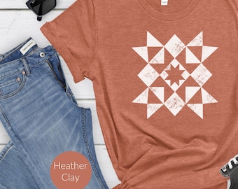 May include: Heather clay-colored t-shirt with a white geometric star pattern. The shirt is styled with blue jeans, black sunglasses, and a pair of black and white sneakers. The shirt is made of a soft, comfortable material.