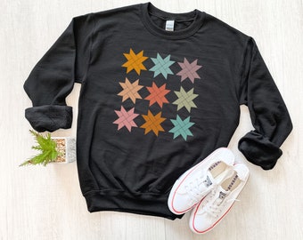 May include: Black sweatshirt with a colorful geometric pattern of stars. The stars are in shades of orange, brown, pink, green, and blue.