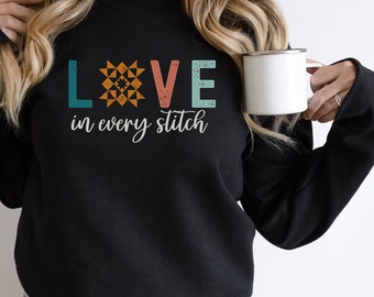 May include: Black sweatshirt with the text "LOVE in every stitch" in a vintage style font. The "O" in LOVE is replaced with a colorful patchwork quilt block.
