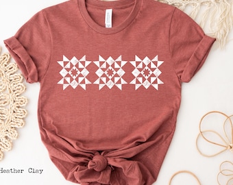 May include: A heather clay-colored t-shirt featuring a white geometric design across the chest. The design consists of three repeating star-like patterns. The shirt is knotted at the waist.