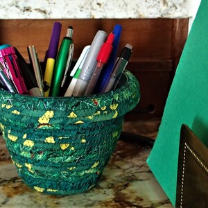 May include: A green fabric pencil holder with a variety of pens and markers inside. The holder is sitting on a marble countertop.