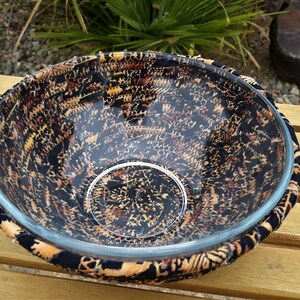May include: A glass bowl with a black and brown patterned fabric cover. The bowl is sitting on a wooden surface.
