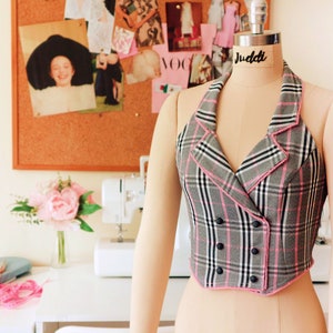 Pu&ograve; includere: Un gilet a quadri bianco e nero con bordi rosa e bottoni neri. Il gilet ha una chiusura a doppio petto e una scollatura halter.