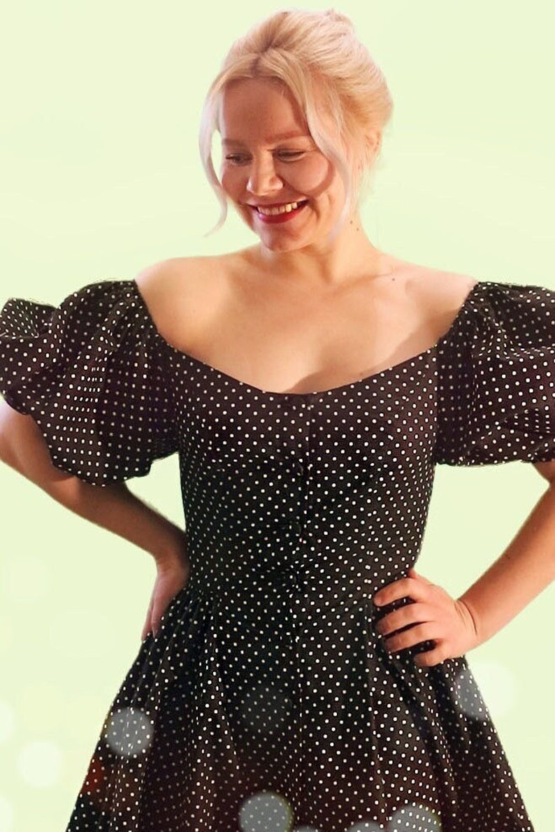 Puede incluir: Una mujer con un vestido de lunares negros y blancos con mangas abullonadas. El vestido tiene un escote de coraz&oacute;n y un corpi&ntilde;o ajustado.