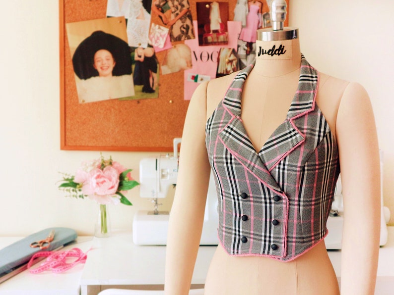 Pu&ograve; includere: Un gilet a quadri bianco e nero con bordi rosa e bottoni neri. Il gilet ha una chiusura a doppio petto e una scollatura halter.