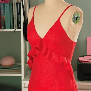 May include: A red sleeveless dress with a ruffled neckline and a floral pattern. The dress is on a mannequin.