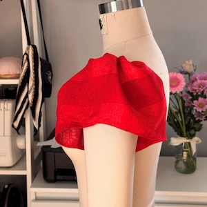 Puede incluir: Una prenda de tela roja con una manga abullonada en un maniquí. La tela tiene un patrón de rayas.