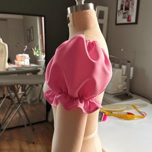May include: A pink fabric puff sleeve with a ruffled edge on a dress form.
