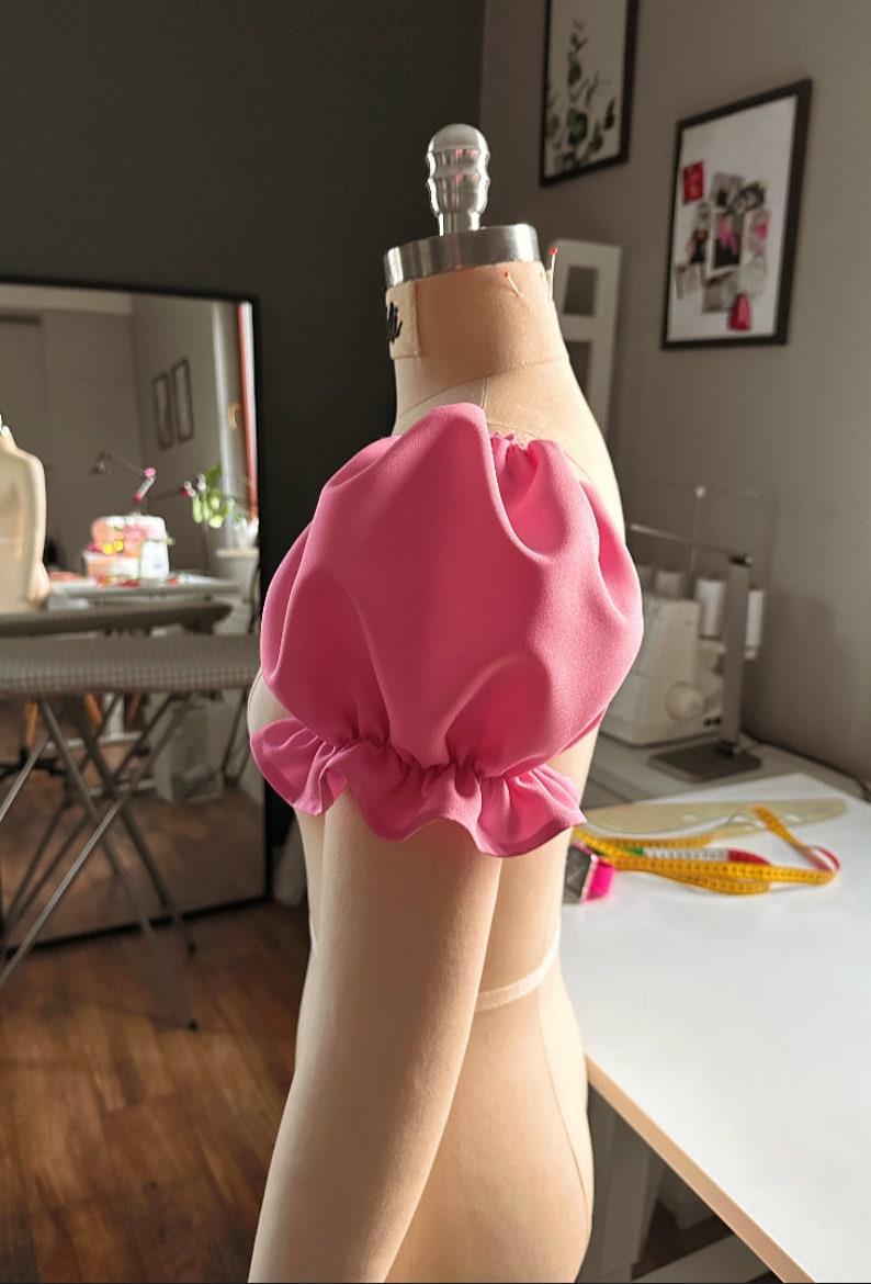 May include: A pink fabric puff sleeve with a ruffled edge on a dress form.