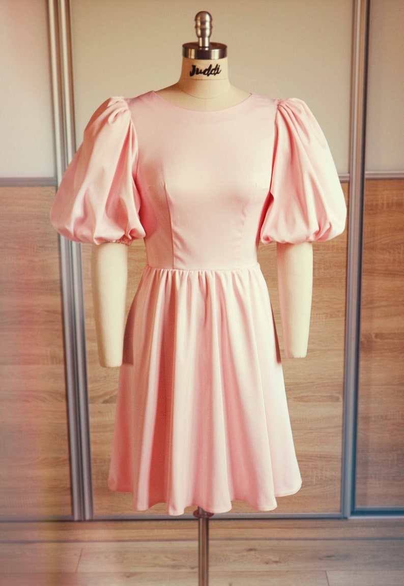 Front view.The top part is fitted.The top consists of one piece.This piece has two breast and two waist darts by design.The skirt is cut off at the waist.The skirt is wide at the bottom. Medium volume.