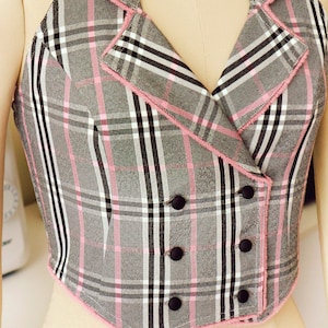 Pu&ograve; includere: Un top halter a quadri grigi e rosa con chiusura a doppio petto e bottoni neri.