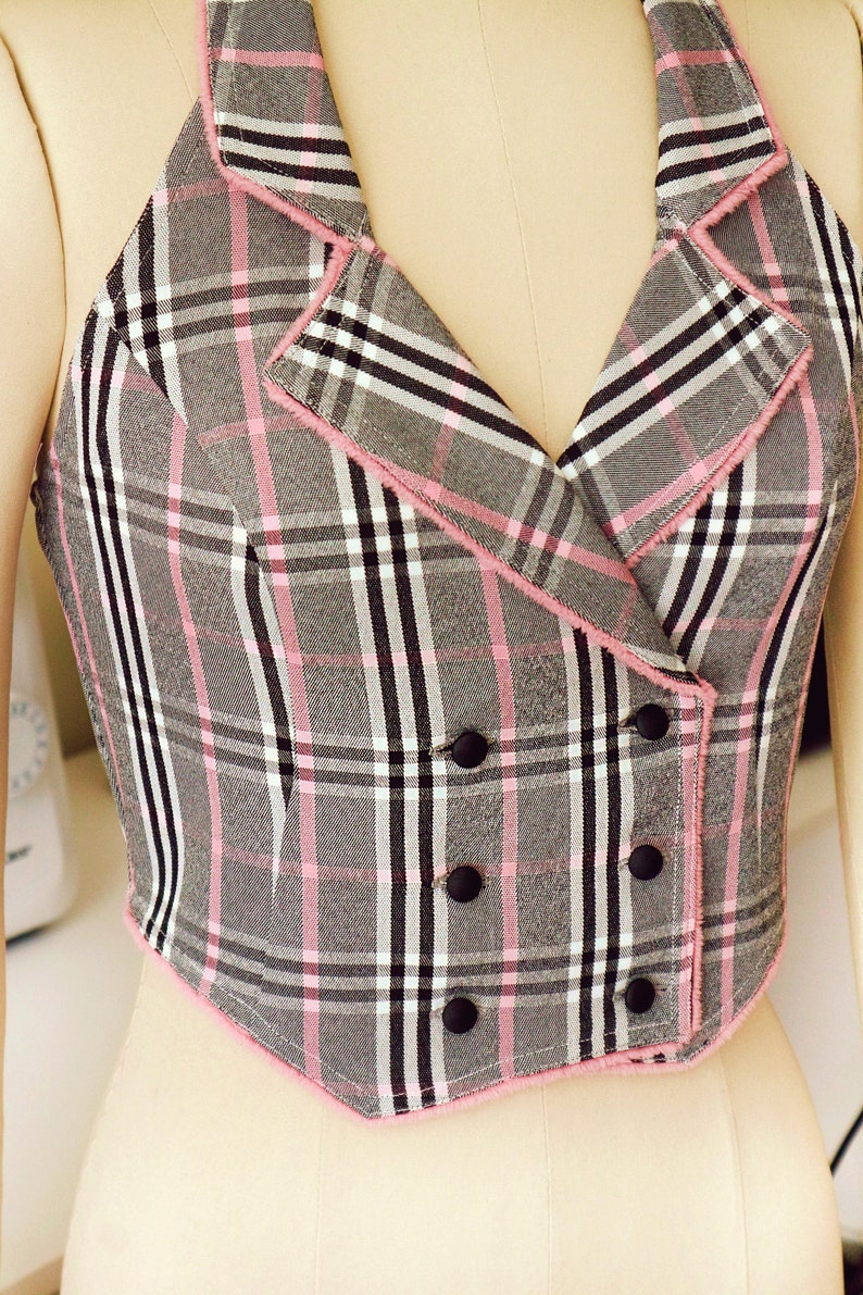 Pu&ograve; includere: Un top halter a quadri grigi e rosa con chiusura a doppio petto e bottoni neri.