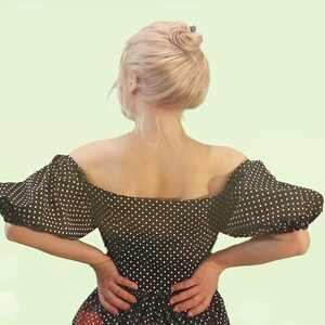 Puede incluir: Una mujer con un vestido de lunares blanco y negro, de hombros descubiertos y mangas abullonadas. El vestido tiene un corpi&ntilde;o ajustado y una falda fluida.