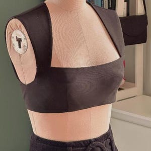 May include: A black sleeveless crop top with a square neckline. The top is on a dress form and is paired with black pants.